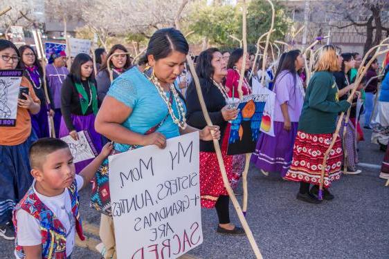 Woman holding sign, "My mom, sisters, aunties + grandmas are sacred'